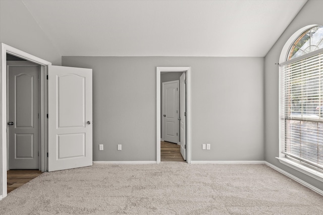 unfurnished bedroom featuring multiple windows, light colored carpet, and lofted ceiling