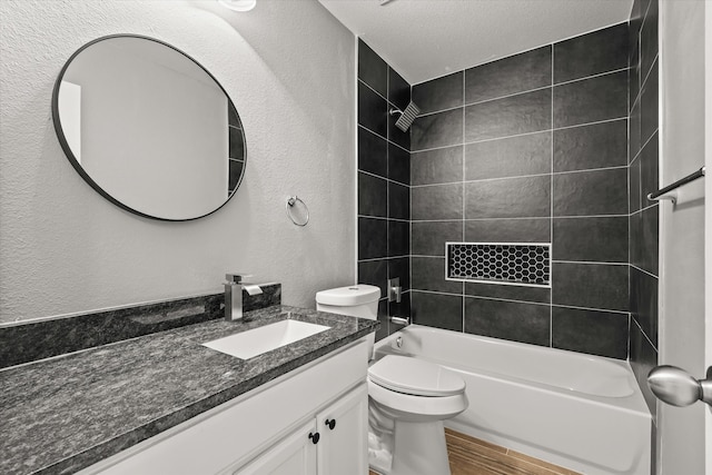 full bathroom featuring a textured ceiling, hardwood / wood-style floors, toilet, tiled shower / bath, and vanity