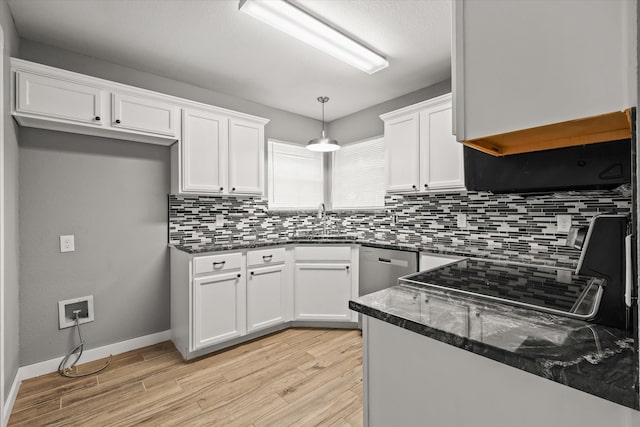 kitchen featuring hanging light fixtures, white cabinetry, light wood-type flooring, dark stone countertops, and sink