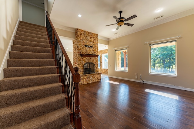 unfurnished living room featuring crown molding, a stone fireplace, dark hardwood / wood-style floors, and ceiling fan