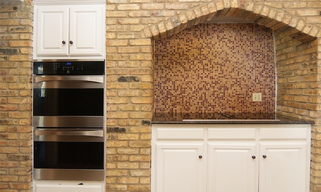 kitchen with brick wall, double oven, and white cabinets