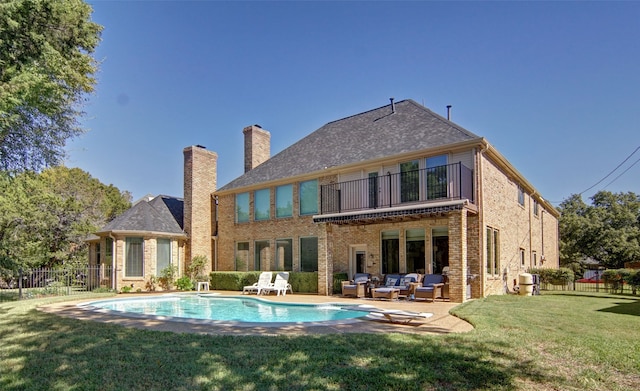 back of property with a balcony, outdoor lounge area, a lawn, a patio area, and a fenced in pool