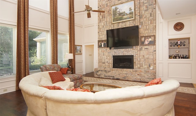 living room featuring a towering ceiling, a fireplace, ceiling fan, crown molding, and dark hardwood / wood-style floors