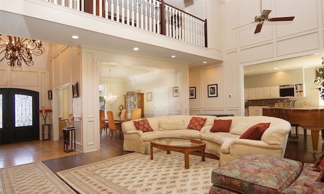 living room with crown molding, hardwood / wood-style flooring, ceiling fan with notable chandelier, and a high ceiling