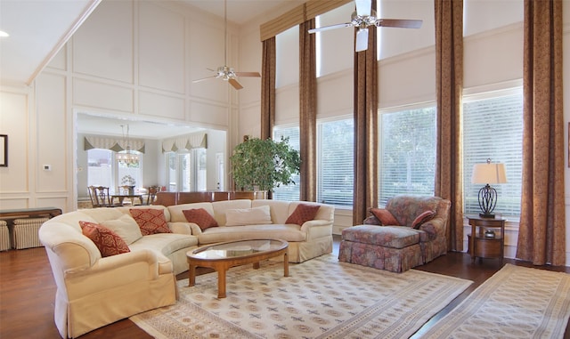 living room with a towering ceiling, hardwood / wood-style flooring, and ceiling fan with notable chandelier