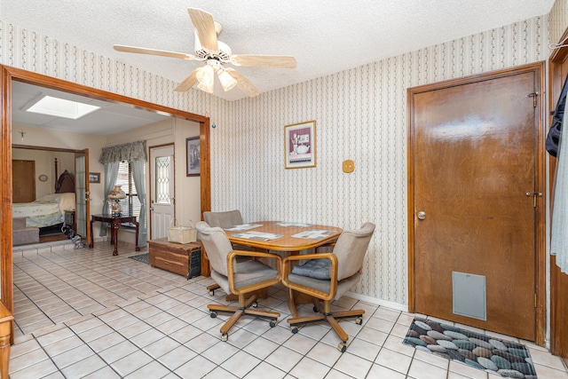 dining space with a textured ceiling, light tile patterned floors, a skylight, and ceiling fan