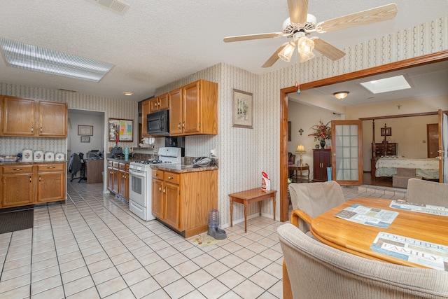 kitchen with light tile patterned flooring, a skylight, a textured ceiling, ceiling fan, and white range with gas cooktop