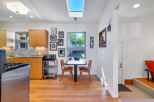 kitchen featuring hanging light fixtures, stainless steel stove, a skylight, light hardwood / wood-style floors, and sink