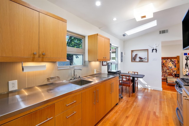 kitchen featuring stainless steel gas range oven, vaulted ceiling with skylight, stainless steel counters, and light wood-type flooring