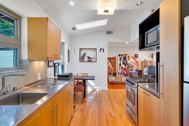 kitchen featuring stainless steel counters, sink, light wood-type flooring, lofted ceiling with skylight, and stainless steel gas range