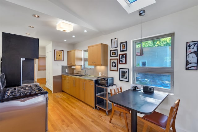 kitchen featuring decorative light fixtures, light wood-type flooring, light brown cabinetry, stainless steel range with gas cooktop, and a skylight