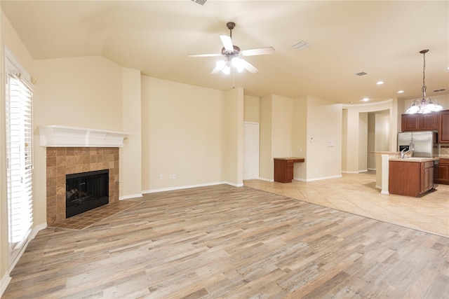 unfurnished living room featuring lofted ceiling, a tiled fireplace, ceiling fan with notable chandelier, and light hardwood / wood-style floors