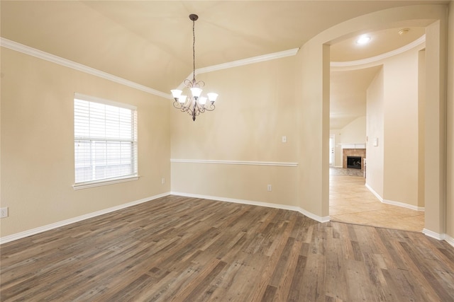 empty room with a tiled fireplace, vaulted ceiling, dark wood-type flooring, ornamental molding, and a chandelier