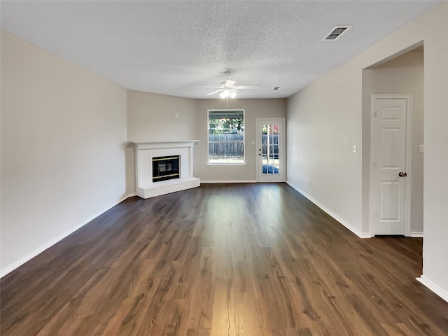 unfurnished living room with a textured ceiling, ceiling fan, dark wood-type flooring, and a brick fireplace