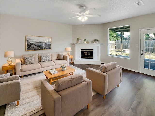 living room with a textured ceiling, a brick fireplace, hardwood / wood-style flooring, and ceiling fan