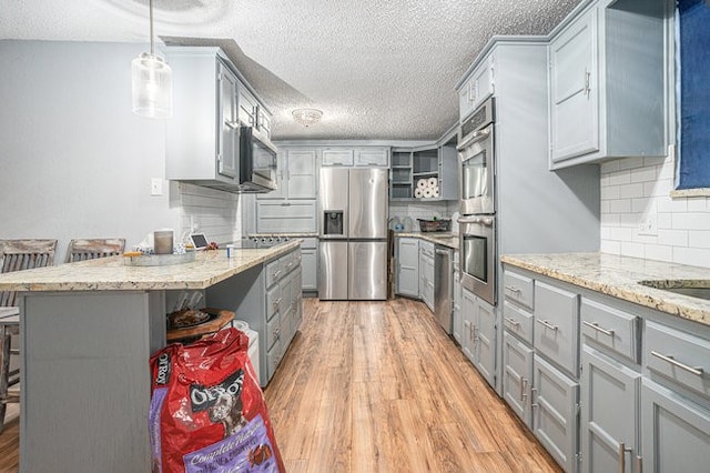 kitchen with hanging light fixtures, backsplash, a breakfast bar area, light hardwood / wood-style flooring, and stainless steel appliances