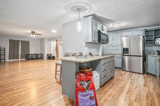 kitchen with a breakfast bar area, appliances with stainless steel finishes, a textured ceiling, light wood-type flooring, and decorative light fixtures