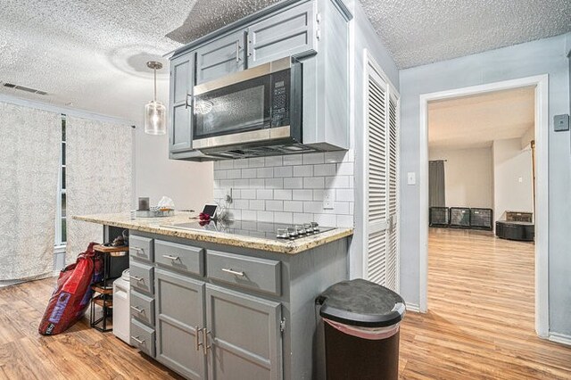 kitchen with light hardwood / wood-style flooring, stainless steel appliances, backsplash, pendant lighting, and a textured ceiling