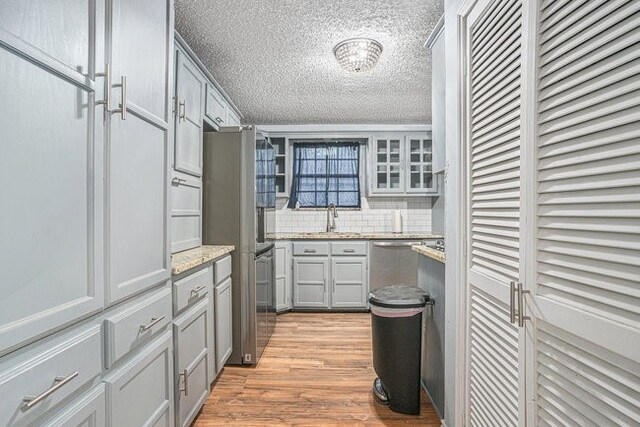 kitchen featuring a textured ceiling, light stone countertops, light wood-type flooring, sink, and stainless steel appliances