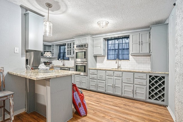 kitchen featuring appliances with stainless steel finishes, backsplash, kitchen peninsula, light hardwood / wood-style floors, and pendant lighting