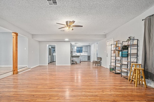 unfurnished living room with decorative columns, light hardwood / wood-style flooring, a textured ceiling, and ceiling fan