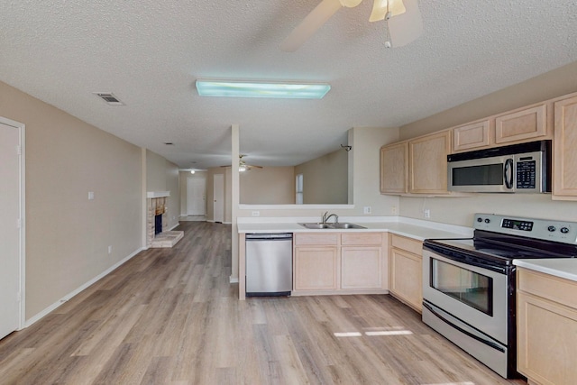 kitchen featuring appliances with stainless steel finishes, a textured ceiling, light brown cabinetry, light hardwood / wood-style floors, and sink