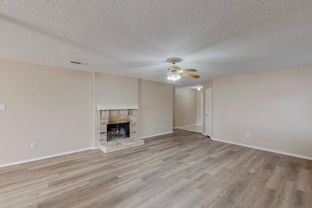 unfurnished living room with light hardwood / wood-style floors, a textured ceiling, a brick fireplace, and ceiling fan