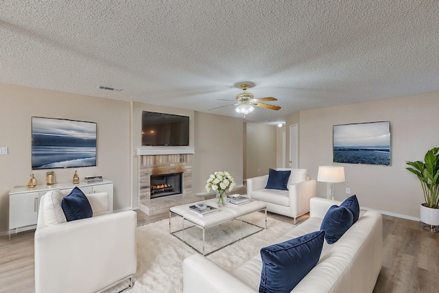 living room featuring a textured ceiling, light hardwood / wood-style flooring, a fireplace, and ceiling fan