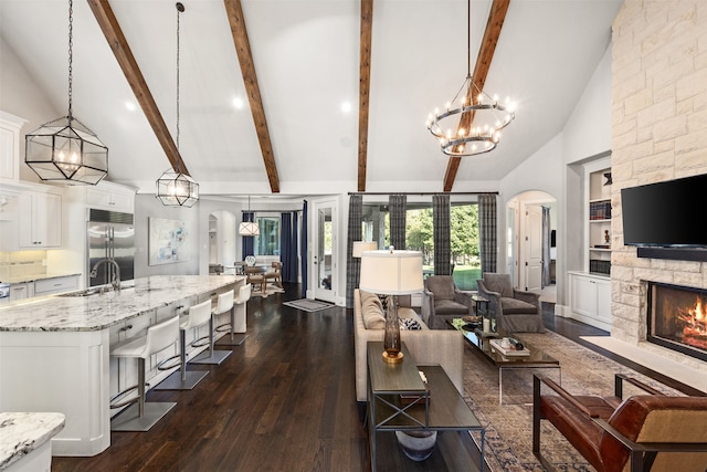 living room featuring sink, a stone fireplace, beamed ceiling, dark wood-type flooring, and high vaulted ceiling