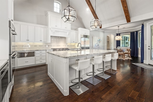 kitchen with a center island with sink, appliances with stainless steel finishes, white cabinetry, high vaulted ceiling, and pendant lighting