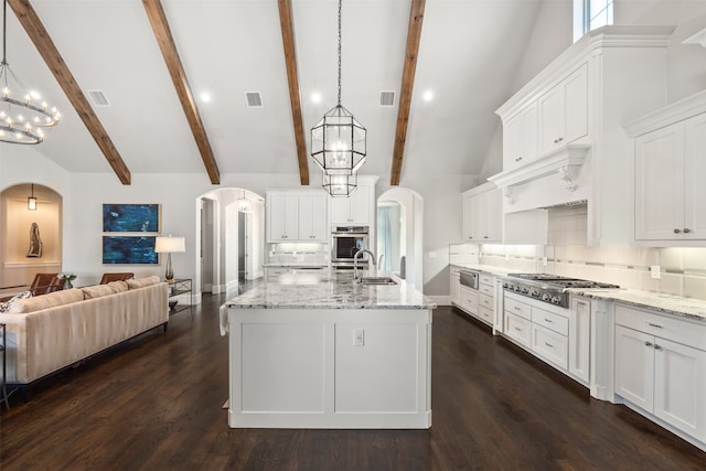 kitchen with stainless steel gas cooktop, a center island with sink, beamed ceiling, and hanging light fixtures