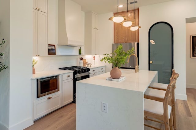 kitchen featuring a center island with sink, appliances with stainless steel finishes, premium range hood, white cabinetry, and pendant lighting