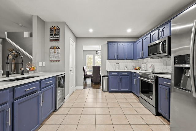 kitchen featuring beverage cooler, sink, blue cabinetry, appliances with stainless steel finishes, and light tile patterned floors