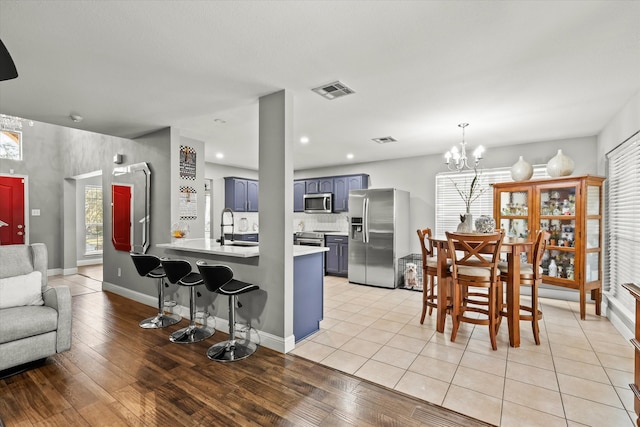 kitchen featuring blue cabinetry, stainless steel appliances, an inviting chandelier, light hardwood / wood-style flooring, and kitchen peninsula