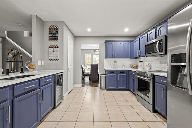 kitchen featuring sink, light tile patterned floors, appliances with stainless steel finishes, wine cooler, and blue cabinets