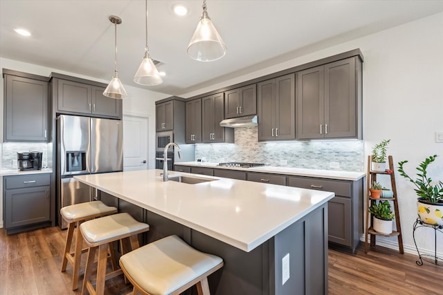 kitchen with pendant lighting, dark wood-type flooring, a kitchen island with sink, and stainless steel appliances