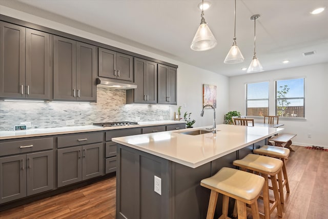 kitchen featuring a kitchen island with sink, stainless steel gas cooktop, sink, pendant lighting, and dark hardwood / wood-style flooring