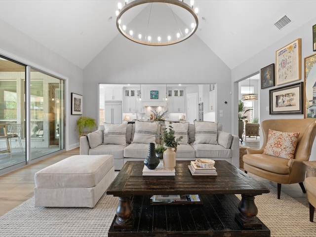 living room featuring a notable chandelier, light wood-type flooring, and high vaulted ceiling