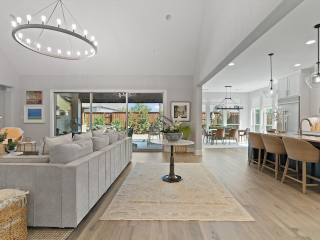 living room with sink, a notable chandelier, high vaulted ceiling, and light wood-type flooring