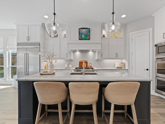 kitchen featuring built in appliances, an island with sink, and white cabinets