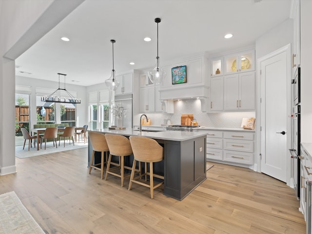 kitchen with light wood-type flooring, plenty of natural light, a center island with sink, and white cabinets