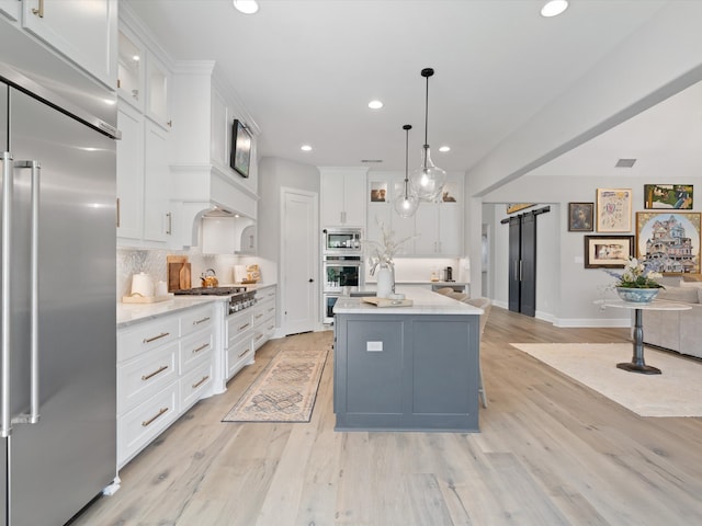 kitchen featuring an island with sink, white cabinetry, a barn door, built in appliances, and pendant lighting