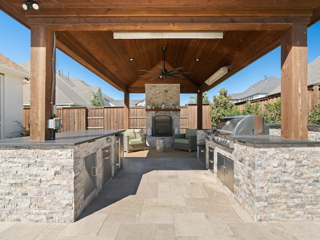 view of patio / terrace featuring area for grilling, an outdoor stone fireplace, exterior kitchen, ceiling fan, and a gazebo