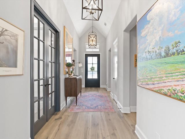 doorway with french doors, a notable chandelier, high vaulted ceiling, and light wood-type flooring