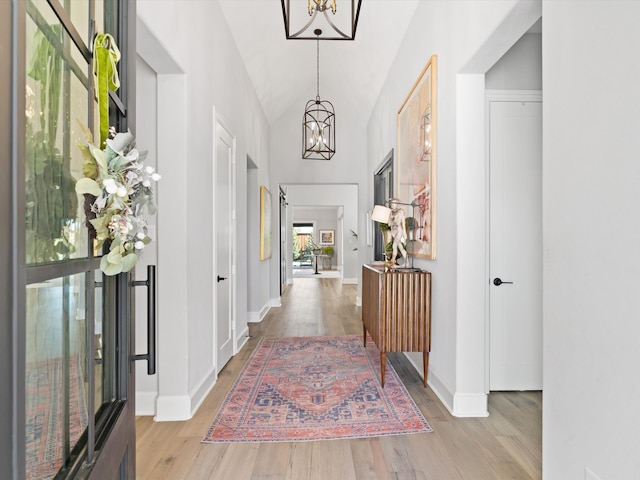 corridor featuring an inviting chandelier, light wood-type flooring, and vaulted ceiling