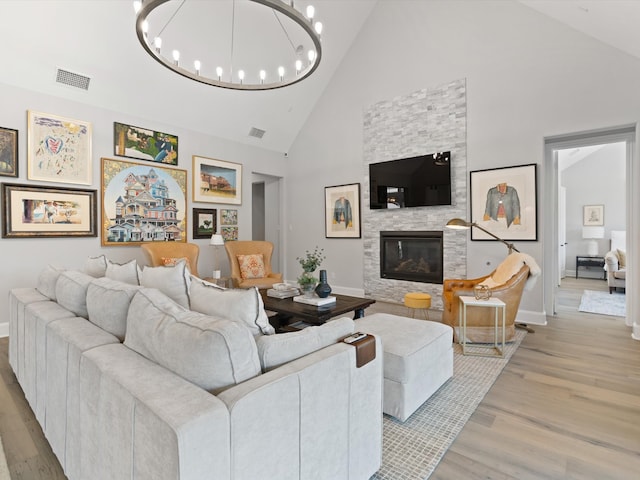 living room featuring light hardwood / wood-style floors, an inviting chandelier, a stone fireplace, and high vaulted ceiling