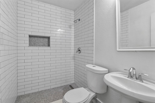 bathroom featuring toilet, sink, and a tile shower