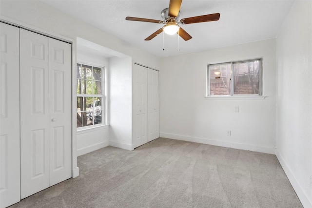 unfurnished bedroom featuring multiple closets, light carpet, and ceiling fan