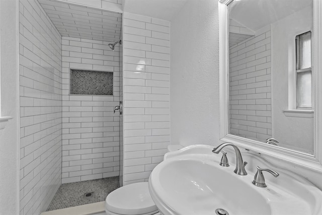 bathroom with toilet, sink, and tiled shower