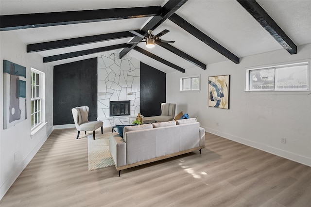 living room with ceiling fan, lofted ceiling with beams, light wood-type flooring, and a fireplace